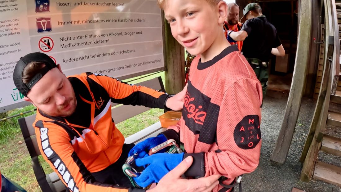 Ben wird der Klettergurt angelegt