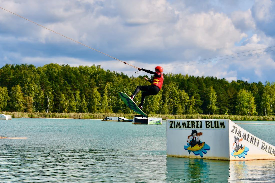 Flo macht einen Sprung mit dem Wakeboard im Wake and Beach