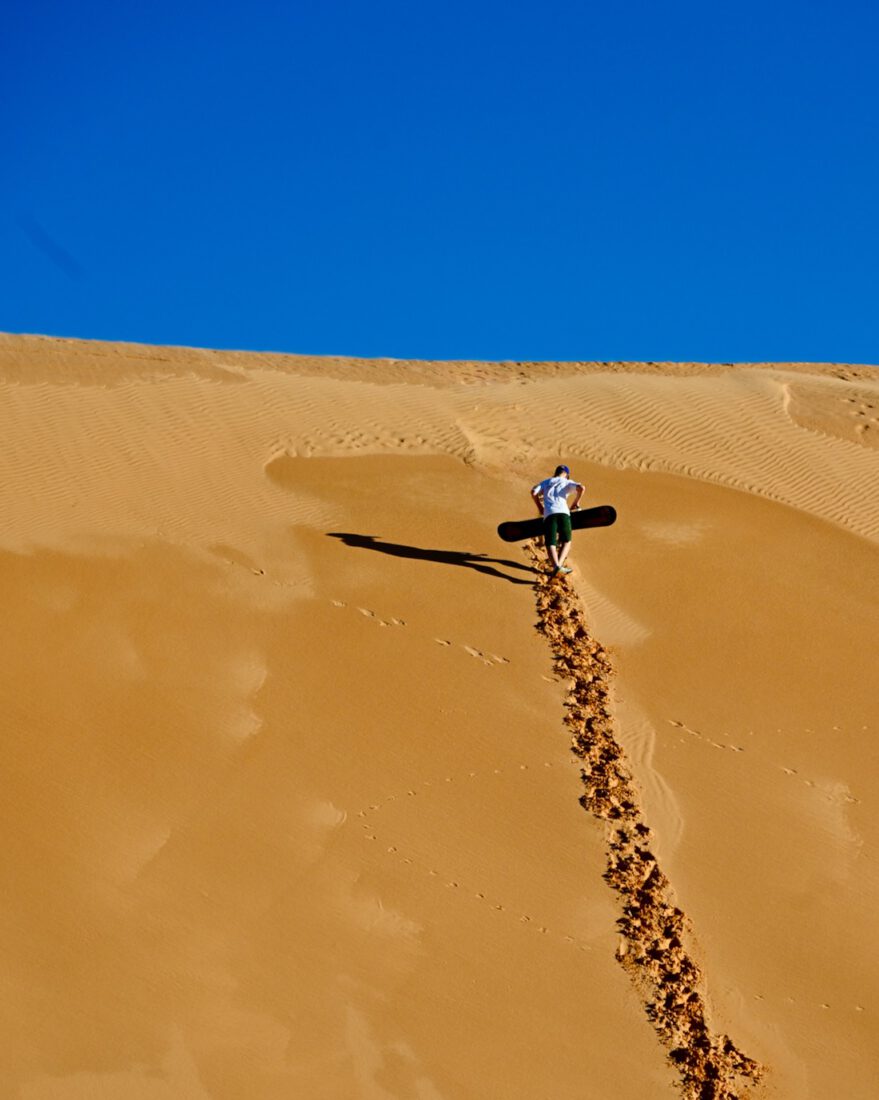 Ben klettert mit dem Sandboard die Dühne in der Sahara hinauf
